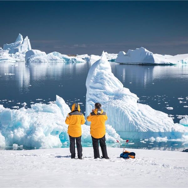 Two guests in yellow parkas admire and photograph rugged icebers off the waters of Port Charcot during a sunny afternoon in Antarctica. Witness ice in all shapes and forms! 